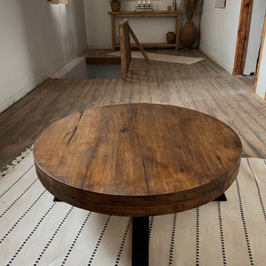 K&ouml;nnte beinhalten: Ein runder Holz-Couchtisch mit einer dunkelbraunen Beize. Der Tisch hat eine dicke, rustikale Tischplatte und ein schwarzes Metallgestell mit vier Beinen.