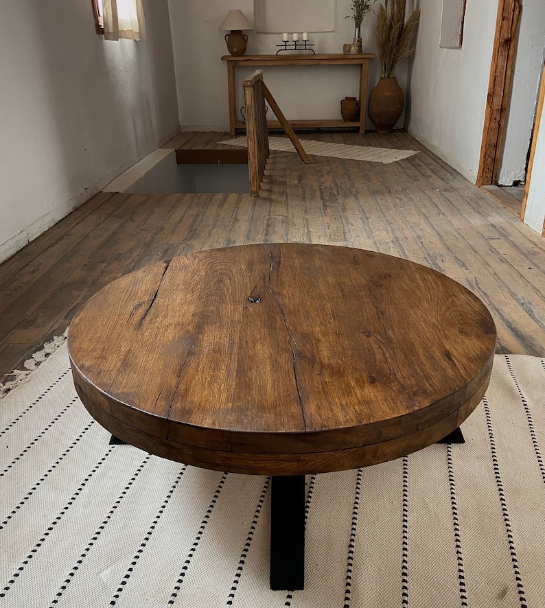 K&ouml;nnte beinhalten: Ein runder Holz-Couchtisch mit einer dunkelbraunen Beize. Der Tisch hat eine dicke, rustikale Tischplatte und ein schwarzes Metallgestell mit vier Beinen.
