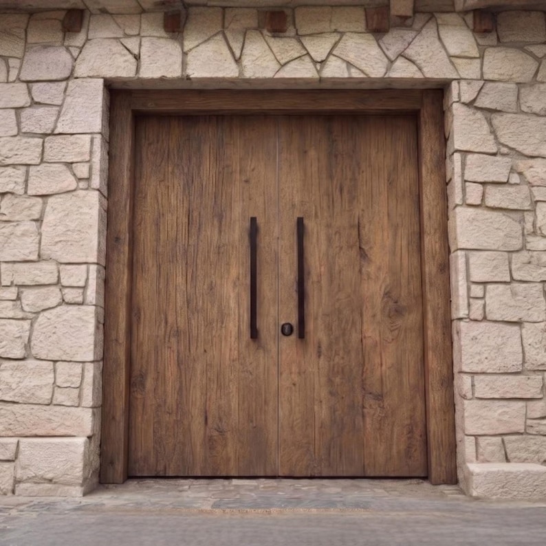 May include: A set of double wooden doors with a natural brown grain finish, featuring two long, vertical black metal handles and a central circular lock. The doors are framed by a wall constructed from light-colored, irregular cut stone blocks.