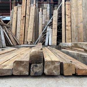 May include: Close-up of reclaimed wood beams, stacked and ready for use in a construction project. The beams are rough-hewn and have a natural, rustic look.