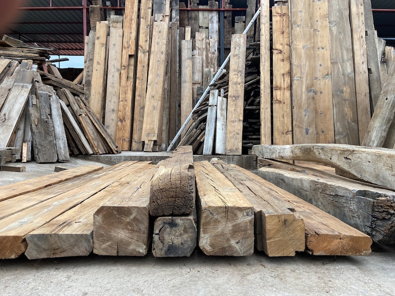 May include: Close-up of reclaimed wood beams, stacked and ready for use in a construction project. The beams are rough-hewn and have a natural, rustic look.