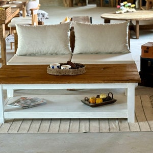 May include: A white coffee table with a wooden top and a lower shelf. The table is sitting on a rug with fringe. There are small decorative pumpkins on the shelf.