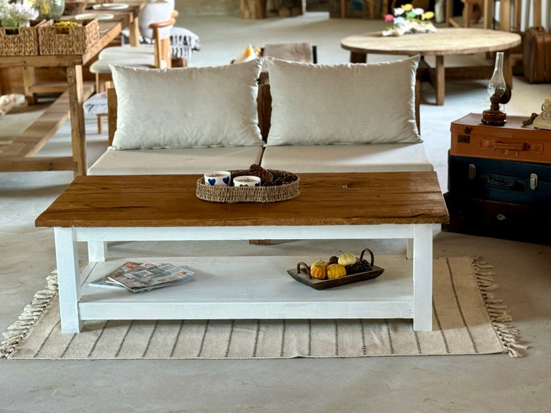 May include: A white coffee table with a wooden top and a lower shelf. The table is sitting on a rug with fringe. There are small decorative pumpkins on the shelf.