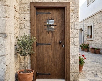 May include: A dark brown wooden door with a vertical wood grain texture, featuring black iron strap hinges, a small square window with a black metal grid, and a round black knob. A rectangular brown doormat sits on the stone ground below.