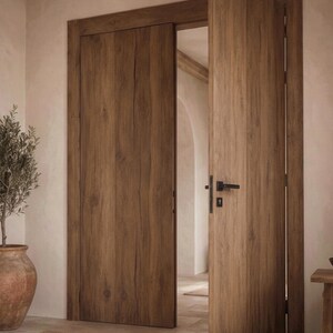 May include: A set of interior doors featuring a medium brown wood grain finish with visible vertical textures. The doors are installed within a matching wooden frame, with one door slightly ajar, revealing a black metal handle and a keyhole plate.