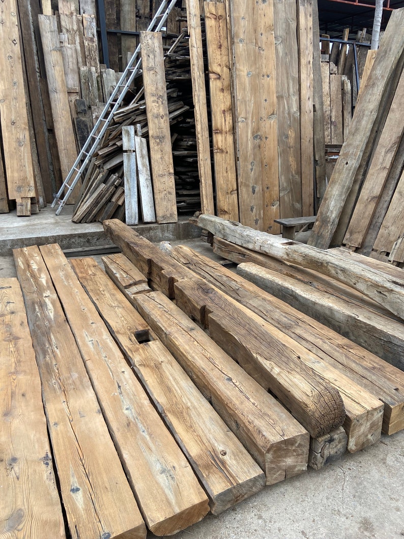 May include: A pile of reclaimed wood beams, stacked and ready for use in a construction project. The beams are weathered and have a rustic appearance.