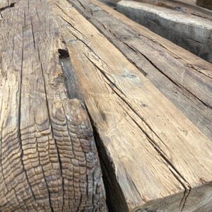 May include: Close-up of a stack of reclaimed wood beams. The wood is weathered and has a natural, rustic look. The beams are perfect for adding a touch of character to any home.