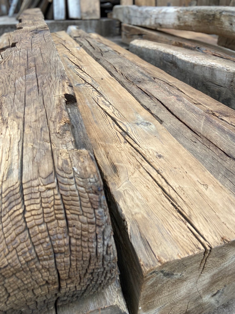 May include: Close-up of a stack of reclaimed wood beams. The wood is weathered and has a natural, rustic look. The beams are perfect for adding a touch of character to any home.