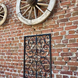 Puede incluir: Decoraci&oacute;n de pared de metal negro con un dise&ntilde;o de desplazamiento. La decoraci&oacute;n est&aacute; montada en una pared de ladrillo con dos ruedas de carro de madera.