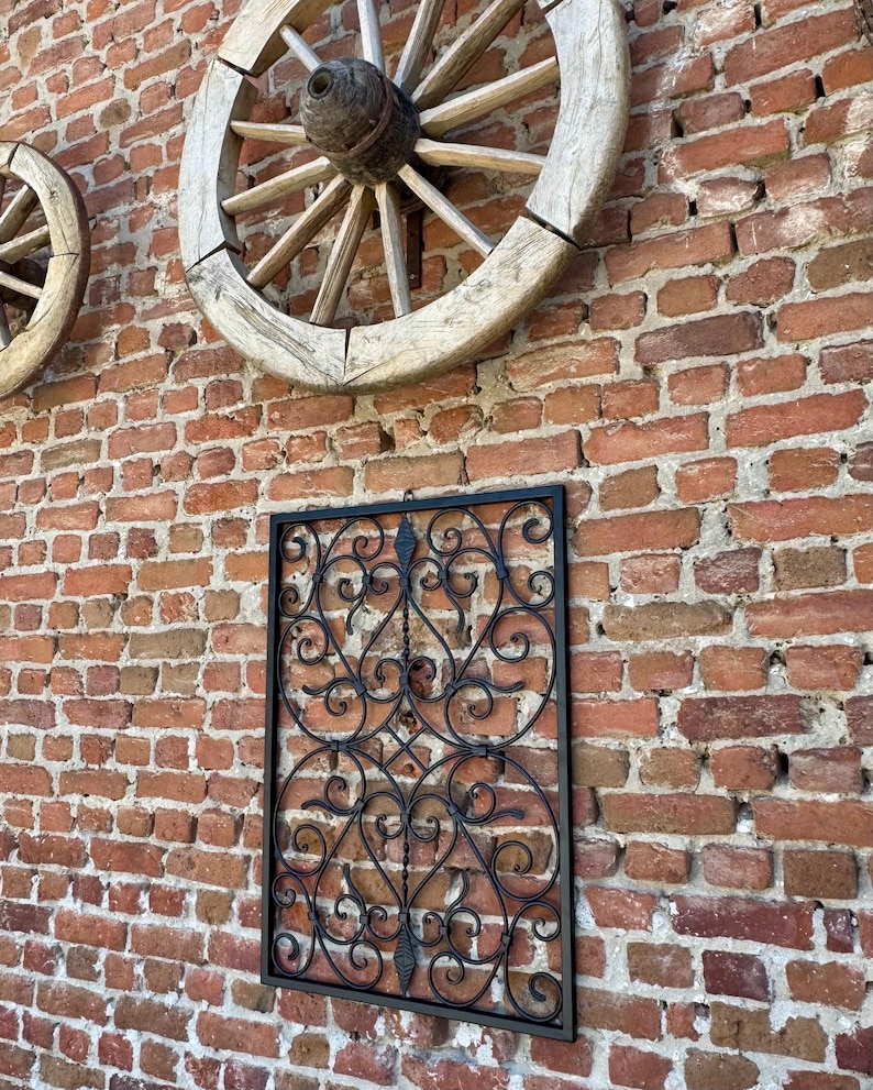 Puede incluir: Decoraci&oacute;n de pared de metal negro con un dise&ntilde;o de desplazamiento. La decoraci&oacute;n est&aacute; montada en una pared de ladrillo con dos ruedas de carro de madera.