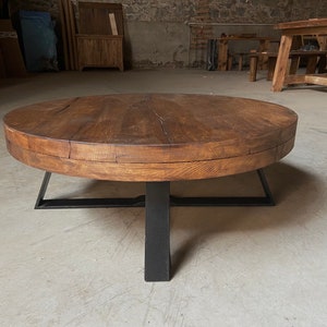 K&ouml;nnte beinhalten: Ein runder Holz-Couchtisch mit dunkelbrauner Oberfl&auml;che und einem schwarzen Metallgestell. Der Tisch hat einen einzigartigen, rustikalen Look und passt perfekt in ein modernes oder industrielles Wohnzimmer.
