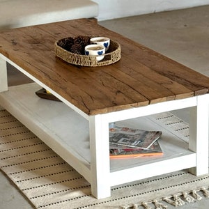 May include: A white coffee table with a wooden top and a lower shelf. The table has a rustic, farmhouse style and is decorated with a woven basket and three small cups.