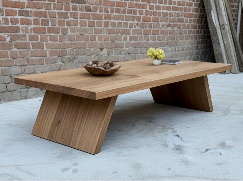 Puede incluir: Una mesa de centro rectangular de madera con patas anguladas. La mesa es de madera clara y tiene un acabado natural. Un cuenco de madera con piedras decorativas y un peque&ntilde;o jarr&oacute;n con flores amarillas est&aacute;n sobre la mesa.