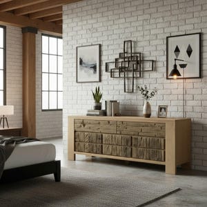 May include: A light wood dresser with a textured front, set against a white brick wall. The room features framed art, a geometric wall sculpture, and a modern lamp. A bed with a black frame is visible in the background.