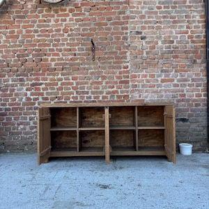 Peut inclure: Un buffet rectangulaire en bois avec une finition marron naturel, dot&eacute; de deux portes battantes aux extr&eacute;mit&eacute;s gauche et droite. L'int&eacute;rieur est divis&eacute; en quatre compartiments de rangement ouverts, chacun &eacute;quip&eacute; d'une &eacute;tag&egrave;re horizontale.