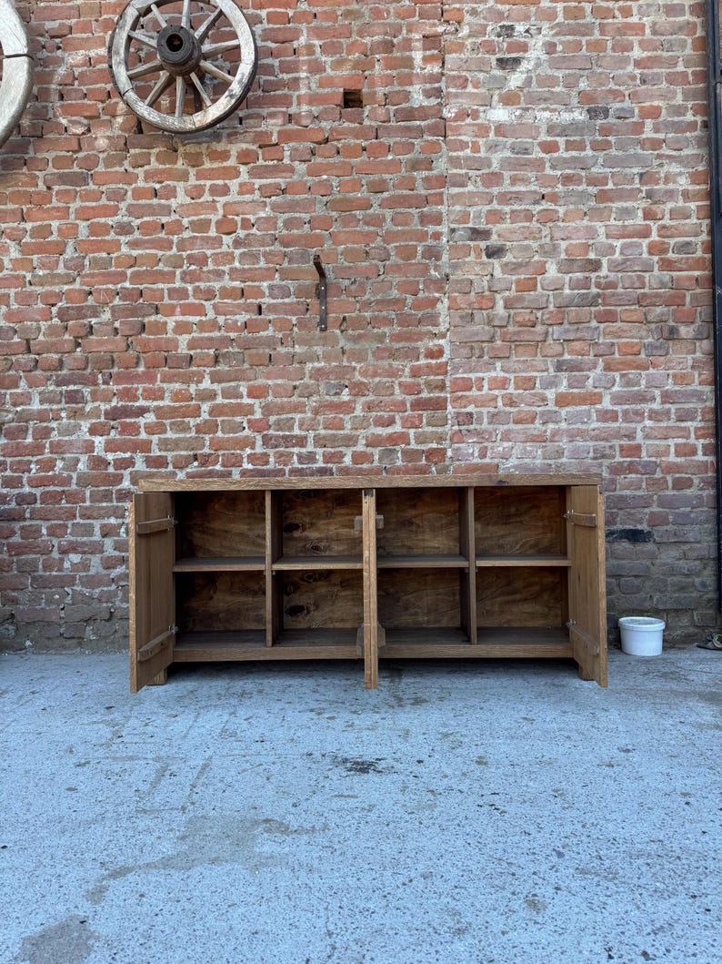 Peut inclure: Un buffet rectangulaire en bois avec une finition marron naturel, dot&eacute; de deux portes battantes aux extr&eacute;mit&eacute;s gauche et droite. L'int&eacute;rieur est divis&eacute; en quatre compartiments de rangement ouverts, chacun &eacute;quip&eacute; d'une &eacute;tag&egrave;re horizontale.