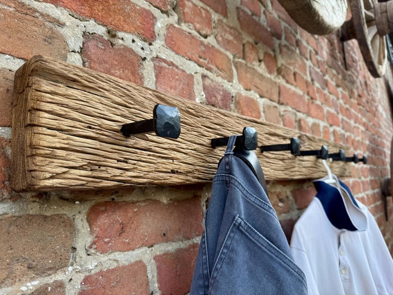 May include: A rustic wooden coat rack with five black metal hooks. The rack is mounted on a brick wall and has a distressed, weathered look.