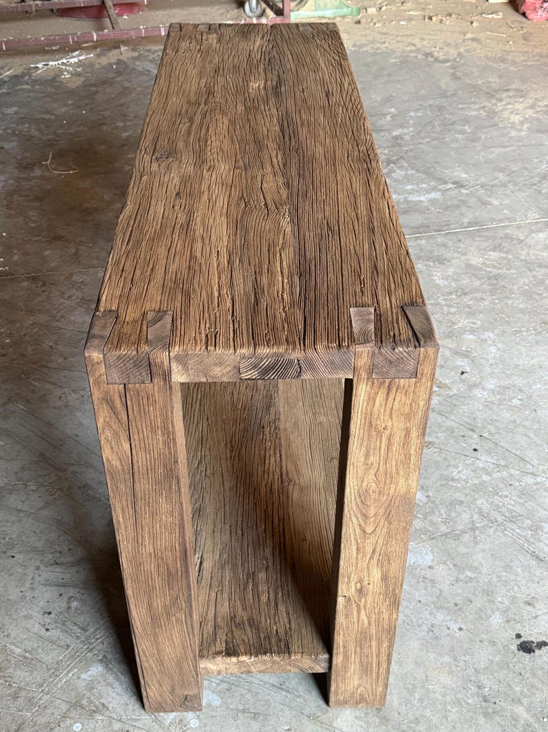 K&ouml;nnte beinhalten: Ein rustikaler Holz-Konsolentisch mit einer nat&uuml;rlichen braunen Oberfl&auml;che. Der Tisch hat ein einzelnes Regal und ist aus recyceltem Holz gefertigt.