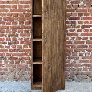 Pode incluir: Um arm&aacute;rio de madeira alto com uma &uacute;nica porta aberta. O arm&aacute;rio tem quatro prateleiras e &eacute; feito de madeira marrom escura.
