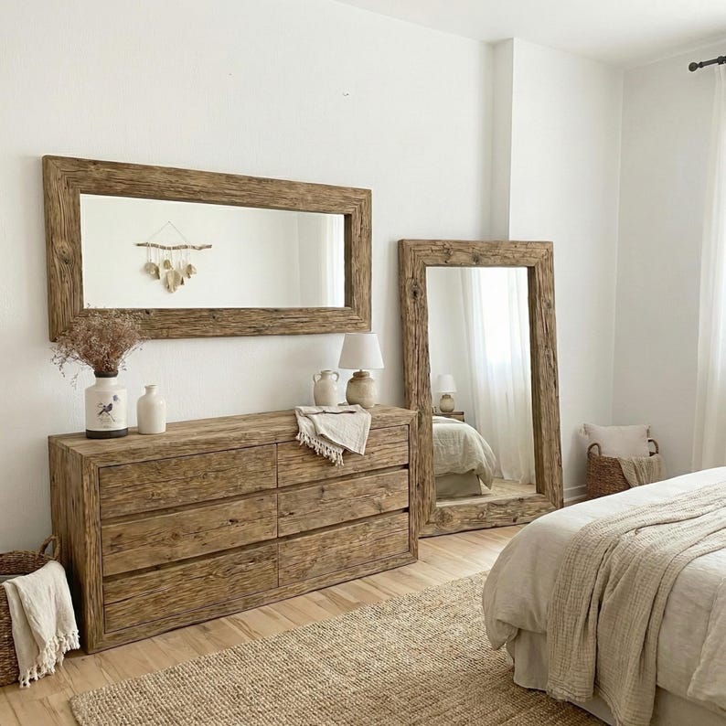 May include: A bedroom scene with a wooden dresser, a large rectangular mirror, and a full-length mirror. The furniture has a natural wood finish. The dresser has six drawers. A woven rug and a bed with neutral-coloured bedding complete the room's decor.