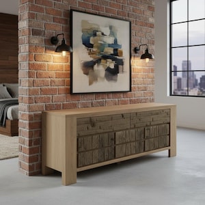 May include: A light wood-toned dresser with six drawers, featuring a rustic, textured wood design on the drawer fronts. The dresser is set against a brick wall with a framed abstract painting and two black sconce lights.