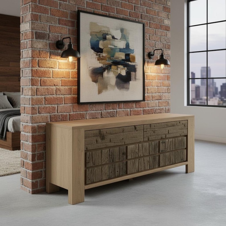 May include: A light wood-toned dresser with six drawers, featuring a rustic, textured wood design on the drawer fronts. The dresser is set against a brick wall with a framed abstract painting and two black sconce lights.