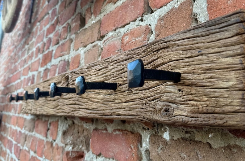 May include: A rustic wooden coat rack with six black metal hooks. The rack is mounted on a brick wall.