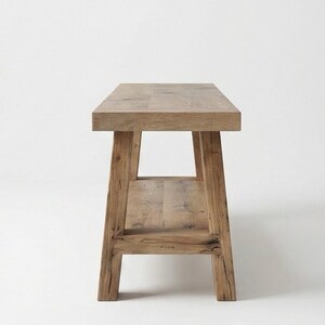 May include: A light brown wooden bench with a rectangular top and a lower shelf. The bench has four sturdy legs and is made of natural wood. The design is simple and rustic, suitable for various interior styles.