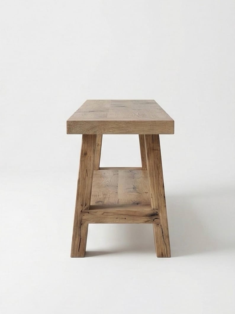 May include: A light brown wooden bench with a rectangular top and a lower shelf. The bench has four sturdy legs and is made of natural wood. The design is simple and rustic, suitable for various interior styles.