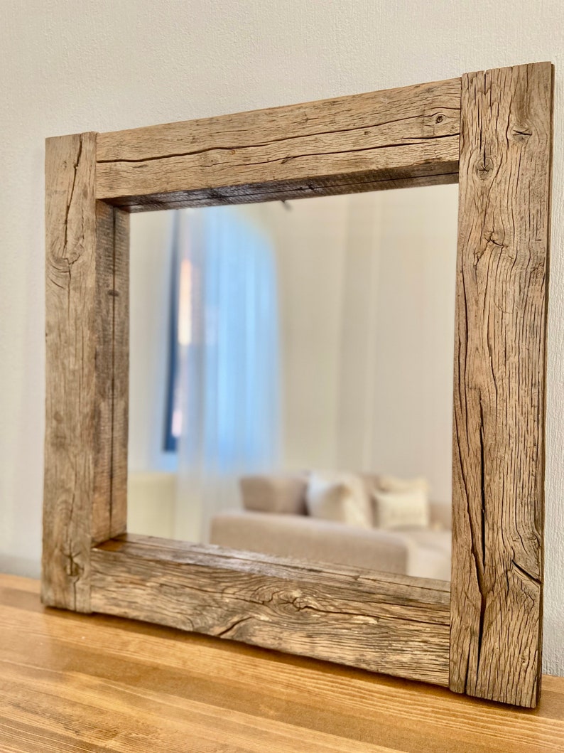 Puede incluir: Un espejo rectangular con un marco de madera r&uacute;stico de color marr&oacute;n claro. El marco est&aacute; hecho de madera gruesa y envejecida con nudos y vetas visibles. El espejo refleja una imagen borrosa de una habitaci&oacute;n con una ventana y muebles.