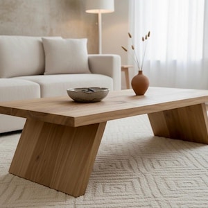 Puede incluir: Una mesa de centro de madera clara con una parte superior rectangular y patas anguladas. Un peque&ntilde;o cuenco de cer&aacute;mica y un jarr&oacute;n de terracota con tallos secos est&aacute;n sobre la mesa. La mesa est&aacute; en un sal&oacute;n con un sof&aacute; blanco y una alfombra estampada.
