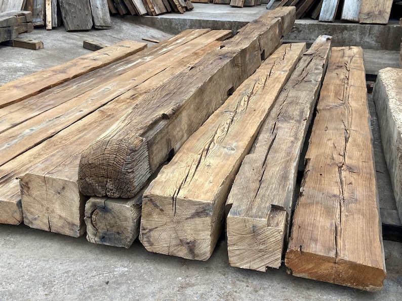 May include: A collection of reclaimed wood beams, showing the natural grain and knots of the wood. The beams are stacked on top of each other, and the ends are cut at an angle. The wood is a light brown color, and the beams are weathered and worn.