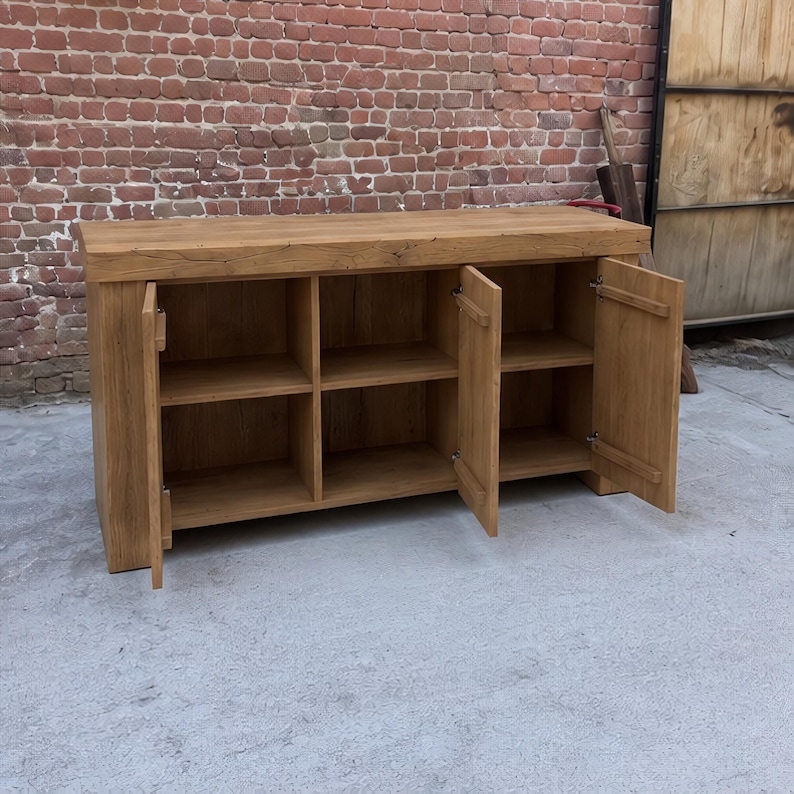 Peut inclure: Un buffet rectangulaire en bois avec une finition naturelle en grain de bois brun clair. Le meuble poss&egrave;de un plateau &eacute;pais et trois sections de rangement ouvertes, chacune divis&eacute;e en deux niveaux par une &eacute;tag&egrave;re, avec deux portes battantes.