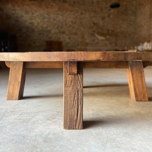 May include: A round wooden coffee table with a rustic finish and four thick legs. The table is made of reclaimed wood and has a natural, weathered look.