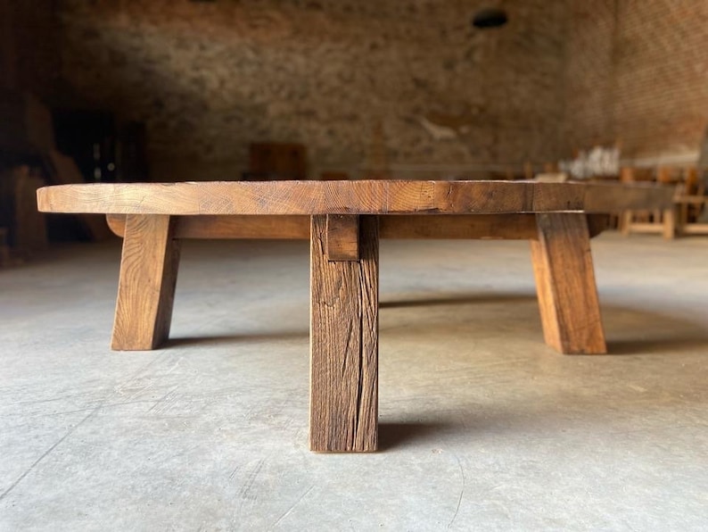 May include: A round wooden coffee table with a rustic finish and four thick legs. The table is made of reclaimed wood and has a natural, weathered look.