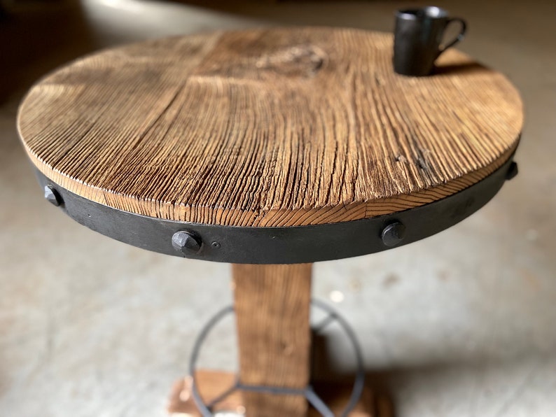 May include: A round wooden table with a black metal band around the edge. The table has a rustic look and is supported by a single wooden leg.