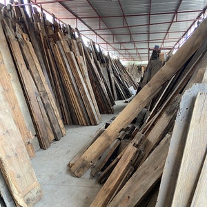 May include: A large pile of reclaimed wood planks in various sizes and shades of brown, stacked in a warehouse setting.