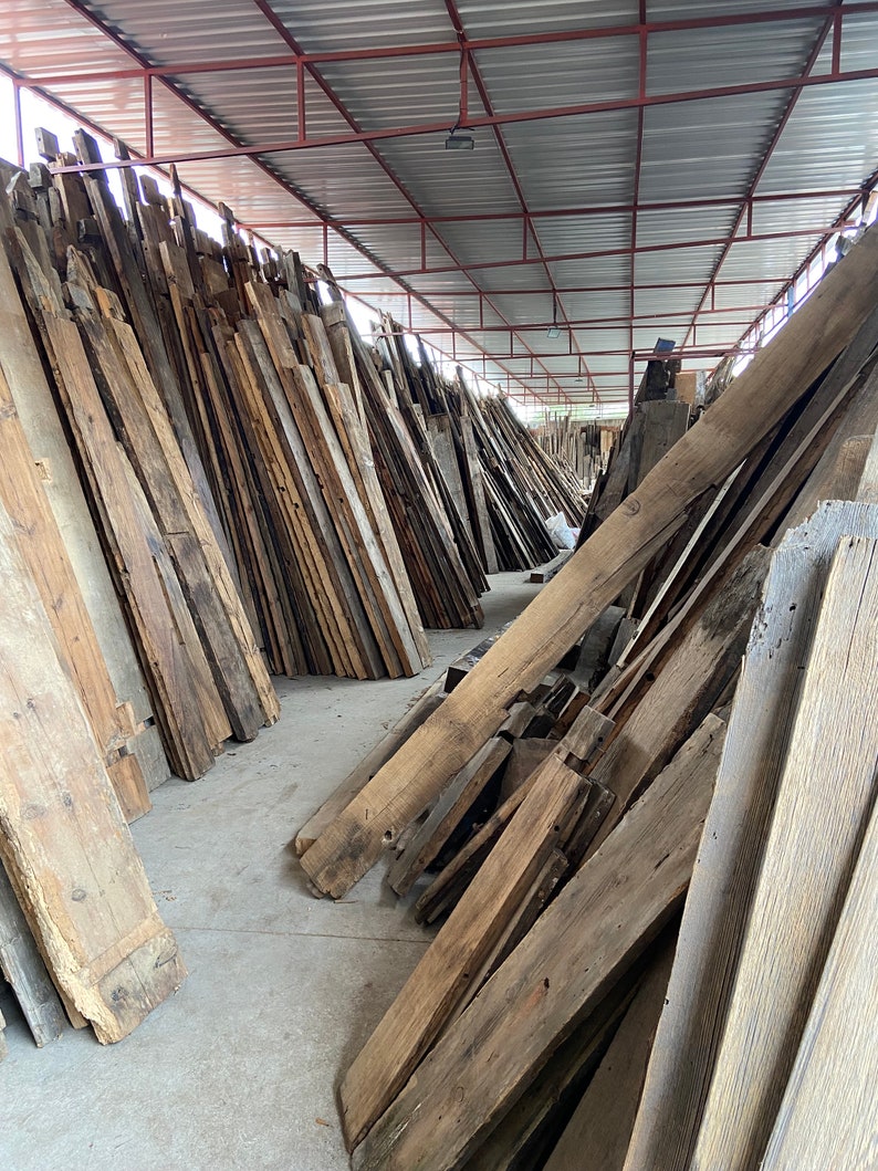 May include: A large pile of reclaimed wood planks in various sizes and shades of brown, stacked in a warehouse setting.