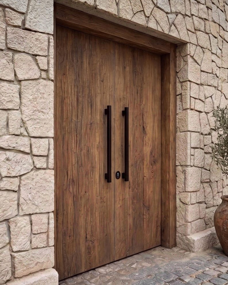 May include: A set of double doors made of dark brown wood with a visible grain pattern. The doors feature two long, vertical, matte black metal handles positioned in the center, along with a small, circular black lock mechanism between them.
