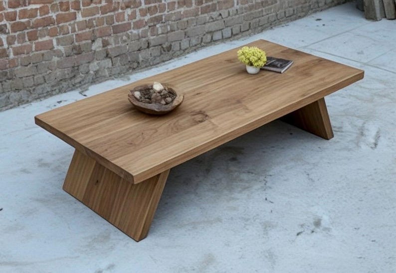 Puede incluir: Una mesa de centro rectangular de madera con acabado natural. La mesa tiene patas anguladas y una superficie lisa. Un cuenco peque&ntilde;o con objetos decorativos, una peque&ntilde;a planta en maceta y un libro est&aacute;n sobre la mesa. La mesa mide unos 152 cm de largo.