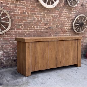 Peut inclure: Un buffet rectangulaire en bois dot&eacute; d'un plateau &eacute;pais et massif ainsi que de trois portes de placard verticales. Le meuble est fabriqu&eacute; en bois brun clair avec un grain visible et une finition lisse, reposant sur une base plate.