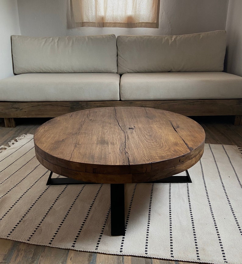 K&ouml;nnte beinhalten: Ein runder Holz-Couchtisch mit einem schwarzen Metallgestell. Die Tischplatte ist aus recyceltem Holz mit einer nat&uuml;rlichen Oberfl&auml;che. Der Tisch steht auf einem wei&szlig;en und schwarzen Teppich.