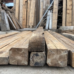 May include: Close-up of four reclaimed wood beams stacked on top of each other. The beams are rough-hewn and have a natural, rustic finish. The wood is a light brown color with dark brown knots and grain patterns.
