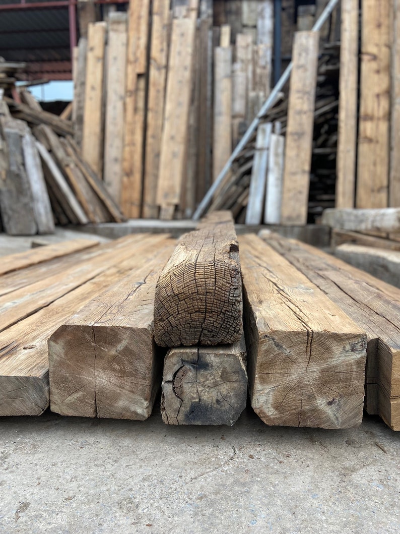 May include: Close-up of four reclaimed wood beams stacked on top of each other. The beams are rough-hewn and have a natural, rustic finish. The wood is a light brown color with dark brown knots and grain patterns.