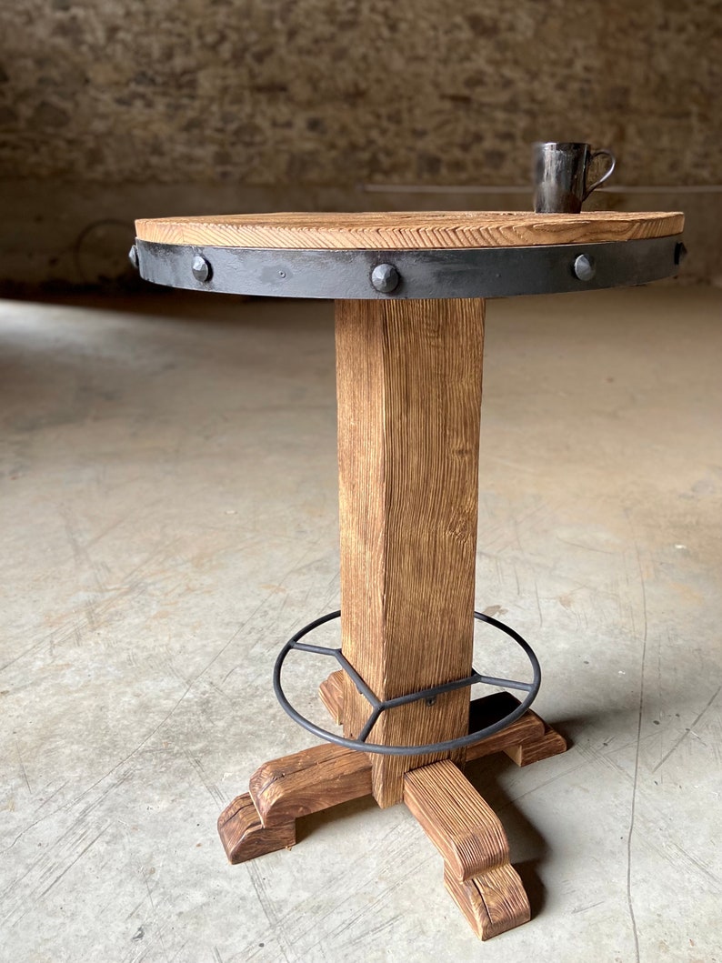 May include: A round wooden table with a black metal rim and studded accents. The table has a single thick wooden leg with a metal footrest and four wooden feet.