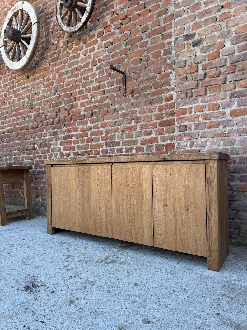 Peut inclure: Un buffet rectangulaire en bois dot&eacute; de quatre portes verticales avec une finition en grain de bois brun clair naturel. Le meuble pr&eacute;sente un plateau &eacute;pais et une structure robuste, offrant un design &eacute;pur&eacute; sans aucune quincaillerie visible.