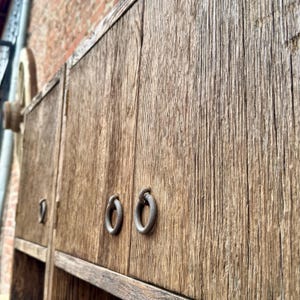 Puede incluir: Primer plano de un armario de madera con dos puertas. Las puertas tienen tiradores de anillo de metal y est&aacute;n hechas de madera recuperada con un acabado r&uacute;stico.