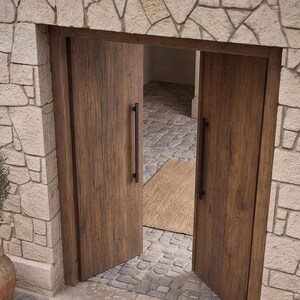 May include: A set of double doors made of medium-brown wood with a visible grain pattern. Each door features a long, vertical, matte black metal handle. The doors are set within a wall constructed of light-colored, irregular-shaped stone blocks.