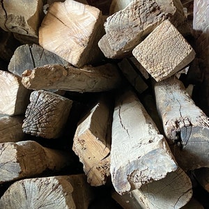 May include: A pile of rough-hewn, weathered wooden beams, showing the natural grain and texture of the wood. The beams are stacked in a haphazard manner, suggesting they are reclaimed or salvaged.