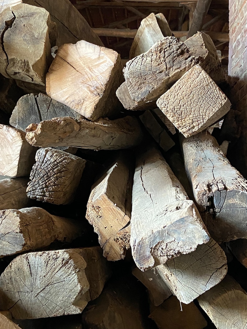 May include: A pile of rough-hewn, weathered wooden beams, showing the natural grain and texture of the wood. The beams are stacked in a haphazard manner, suggesting they are reclaimed or salvaged.